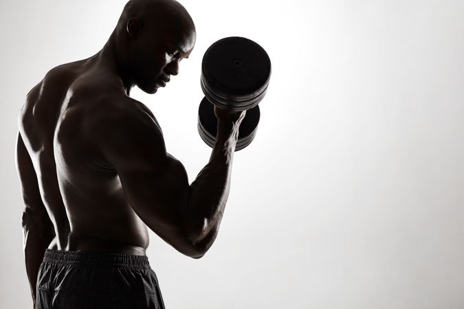 Strong man exercising with heavy dumbbells against grey background