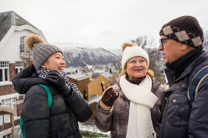 Asian resting female in warm clothing smiling while communicating with locals man and woman at city street