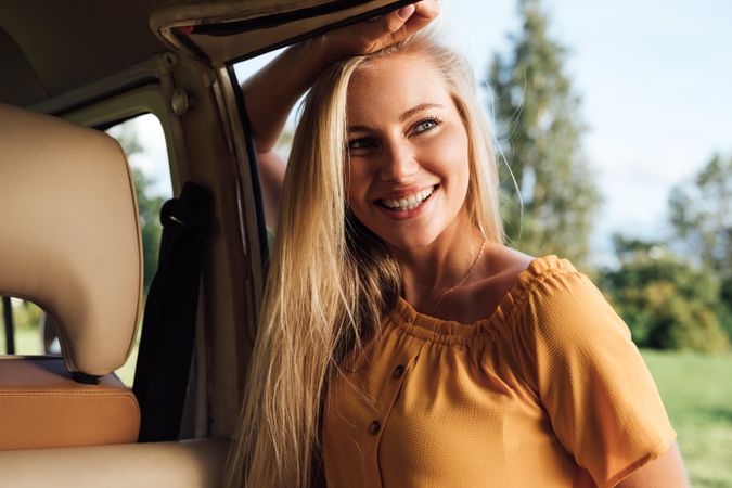Portrait of blonde woman leaning on a van door in a field
