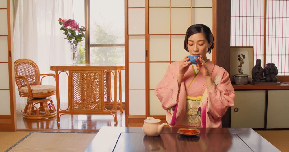 Asian Woman Wearing a Classical Pink Kimono and Sitting Behind a Low Table in a Traditional Japanese Home