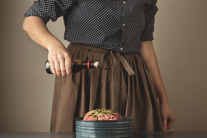 Woman pouring brown liquid onto ground beef