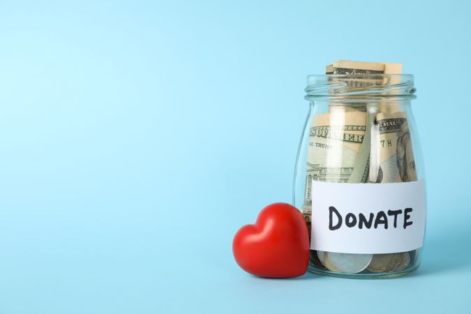 Glass jar with text Donate and heart on blue background