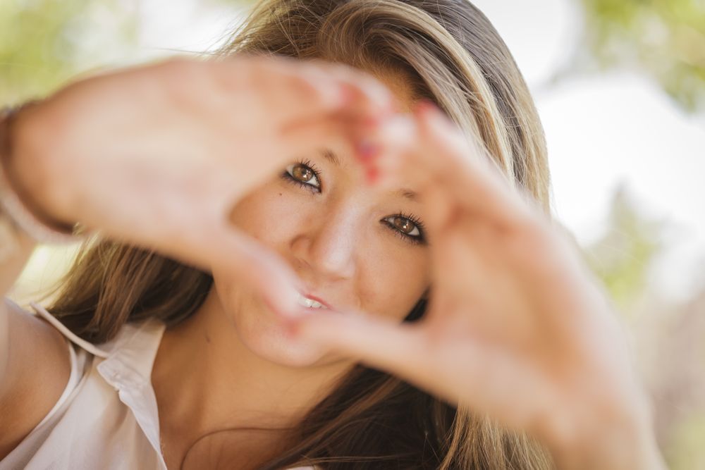 Portrait Of Asian Woman Making Heart Hand Sign Outdoors