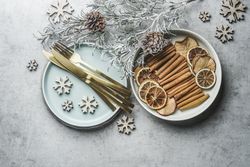 Christmas table setting with golden cutlery, pale blue plate, cinnamon sticks, dried orange natural dried apples and oranges and winter branches on grey table