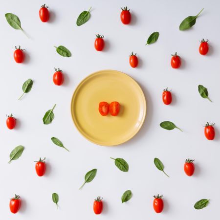 Yellow plate with halved tomato on tomato and basil pattern on light background