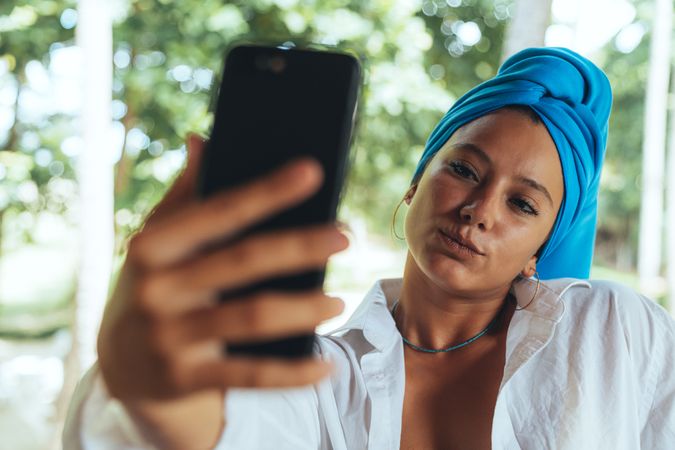 Positive woman with turban on head taking selfie on sunny street