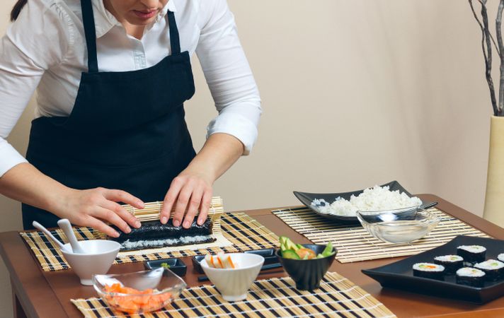 Portrait of chef in apron rolling sushi in nori sheet on table using mat