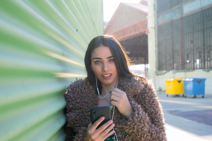 Trendy woman with smartphone near wall