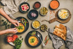 Spread of yellow lentil soup bowls, with bread, and vegetable garnishes with man’s hands over soup