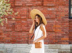 Woman in summer dress & straw hat standing in front of a red brick building