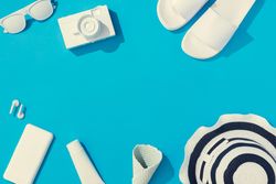 Summer objects of flip flops, sunglasses, camera, smart phone, hat and EarPods on blue background