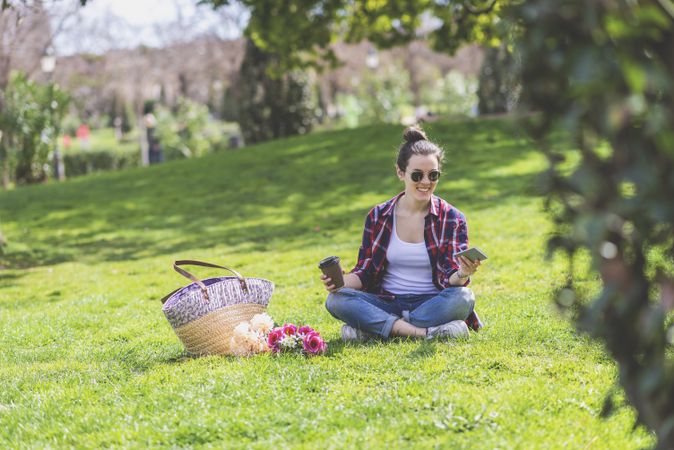 Front view of a young hipster woman sitting on grass in a park