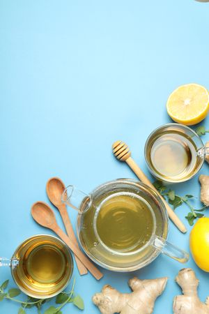 Cups and teapot with tea, lemon, ginger on blue background, space for text