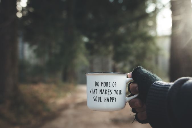 Crop hand with motivational mug in forest