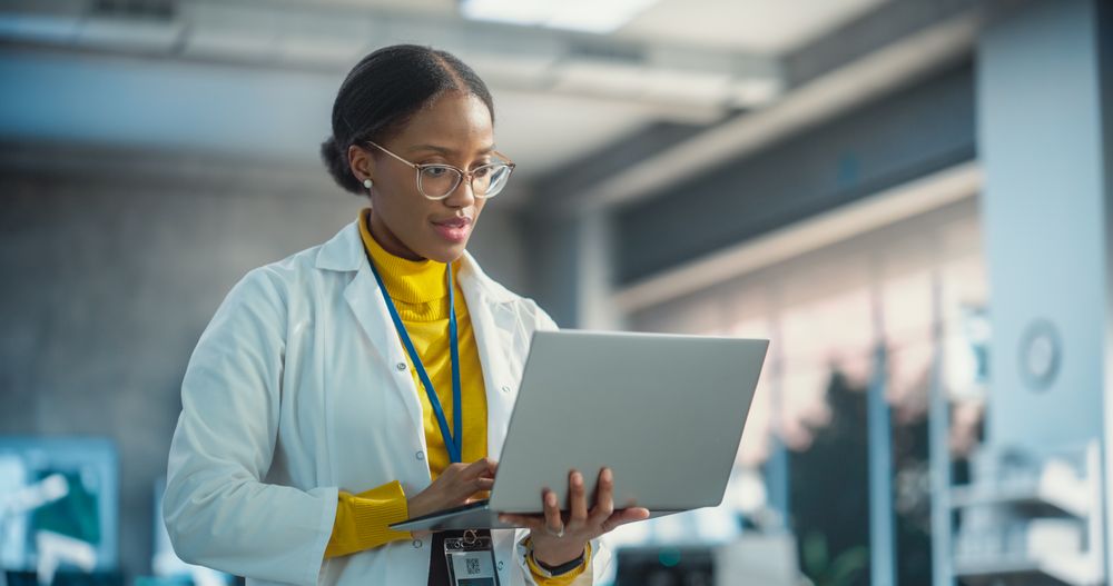 Portrait of Young Black Female Specialist in a Lab Coat Using Laptop.