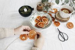 Closeup of woman's hands making Christmas garland with dry oranges fruit and pine, eucalyptus tree branches on linen table cloth
