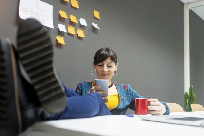 Smiling businesswoman with mug using smartphone