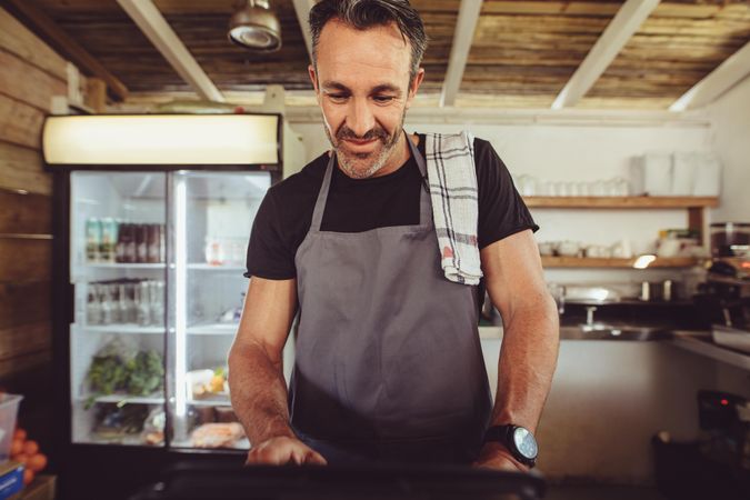 Mature man in apron working a coffee shop computer