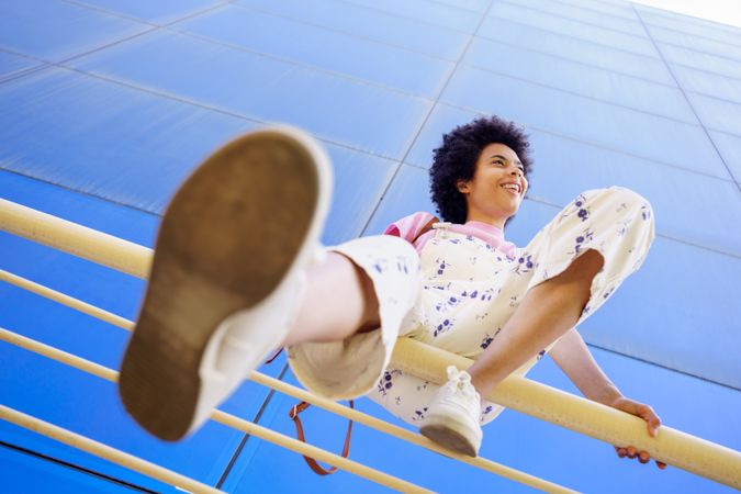 Low angle shot of woman sitting on handrails in front of  reflective glass building on summer day