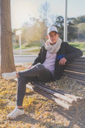 Teenage male sitting on a wooden bench in a city park