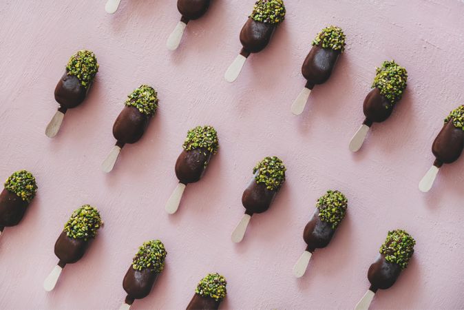 Diagonal rows of ice cream chocolate pistachio popsicles, pink background