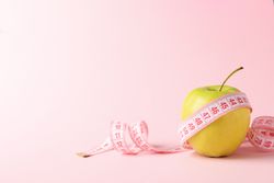 Measuring tape with apple on pink background, weight loss
