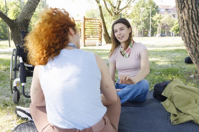 Back of red haired woman chatting with her friend sitting in a park