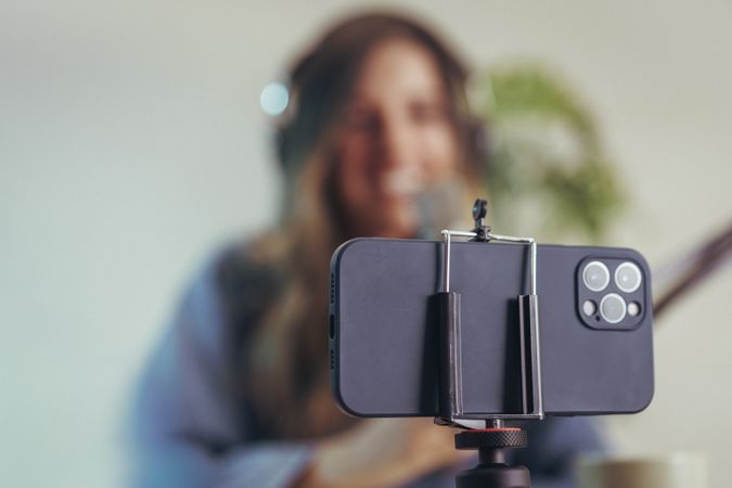 Influencer recording podcast with smartphone on tripod indoors