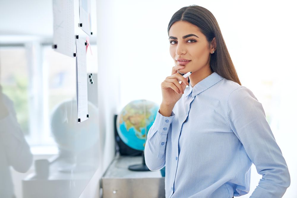 Curious woman brainstorming at dry erase board while looking at camera