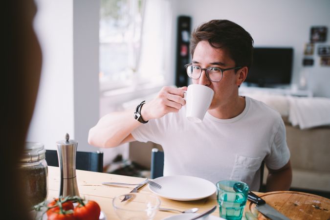 Young man sitting at a breakfast table drinking from a mug