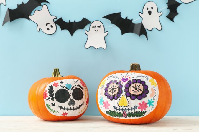 Pumpkins with catrina skull makeup, ghosts and bats on blue background