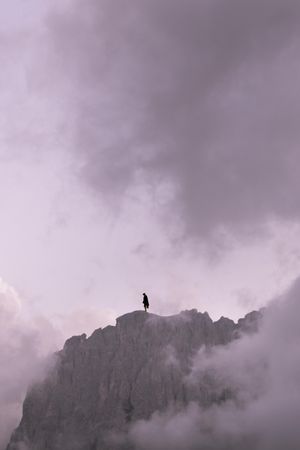 Silhouette of person standing on rock formation under cloudy sky