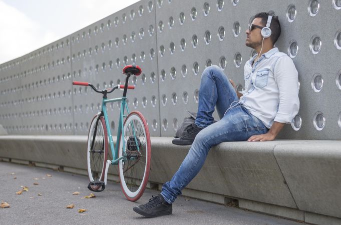 Male in sunglasses relaxing outside of park listening to music with bicycle
