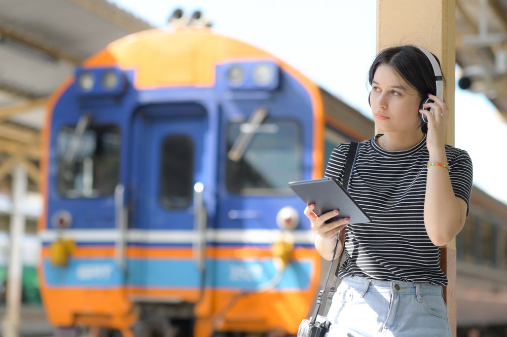 Young woman leaning on a pole at the train platform in headphones