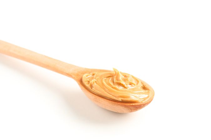 Creamy peanut butter in wooden spoon isolated on light background, closeup. A traditional product of American cuisine