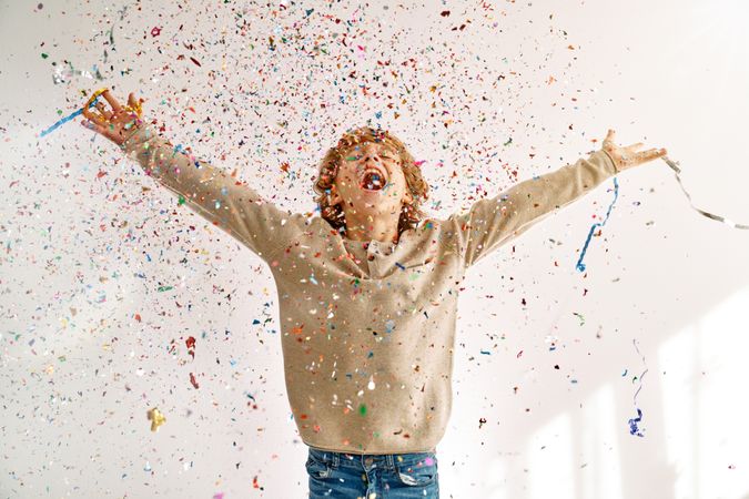 Happy boy enjoying falling confetti and sparkles and shouting jo