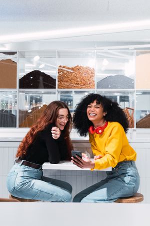 Positive multiethnic female friends using smartphones and laughing in cafe