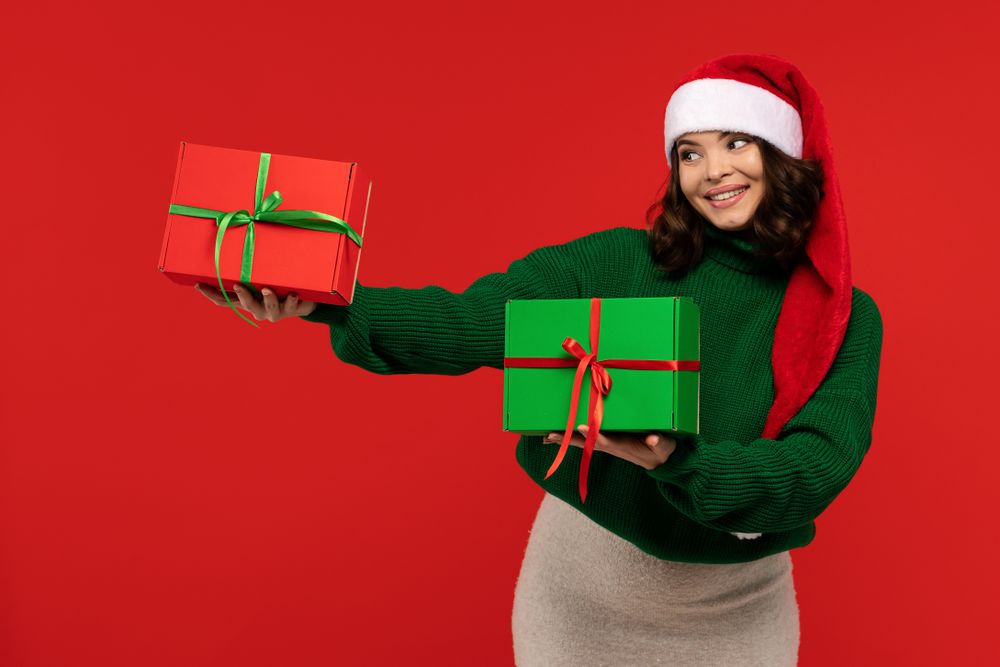 Smiling woman in Santa hat holding Christmas gift boxes.