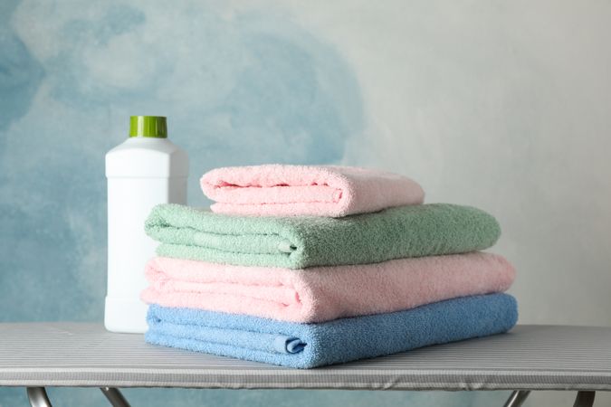 Stack of clean towels and laundry liquid on ironing board, copy space