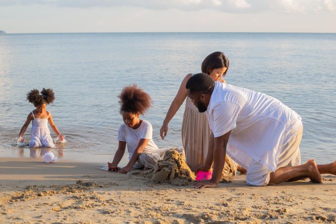 Asian & Black family building sand castle at tropical beach in summer