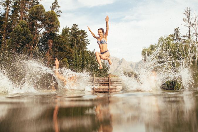 Portrait of young women jumping into a wilderness lake from the jetty