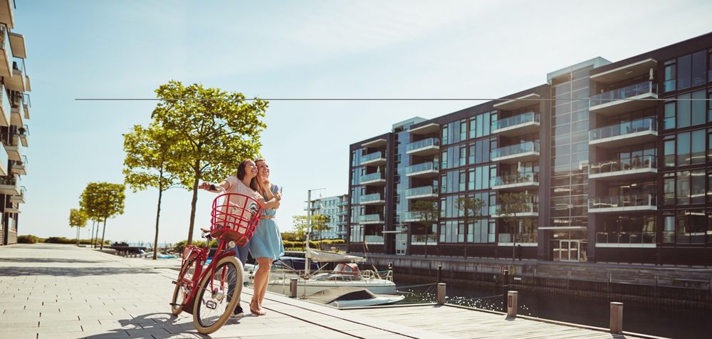 Two women laughing while walking with a bicycle along the river walk, copy space