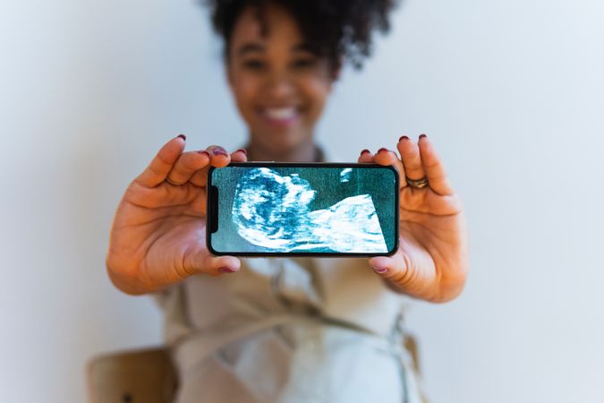 Smiling Black woman showing smartphone screen with baby ultrasound