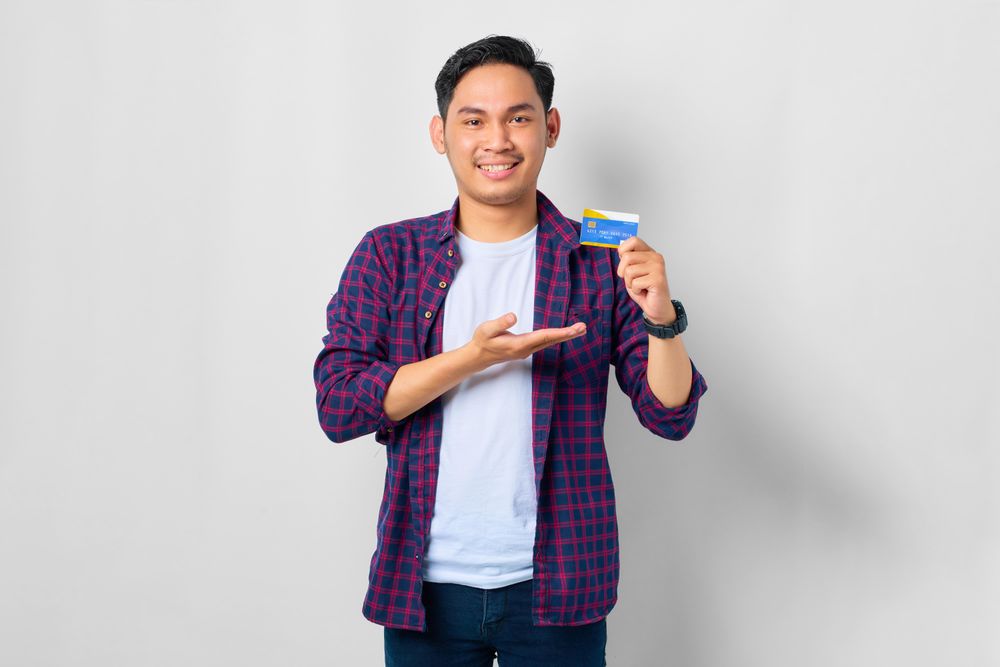Asian male in grey studio presenting credit card