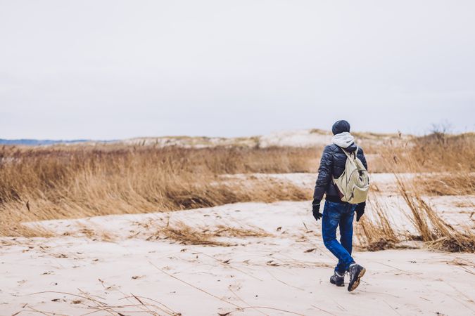 Man walking between sand field with dry grass
