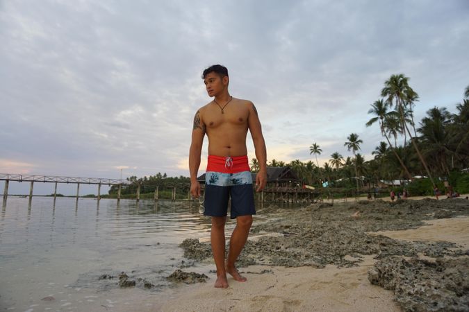 Topless man in swimwear shorts standing on beach