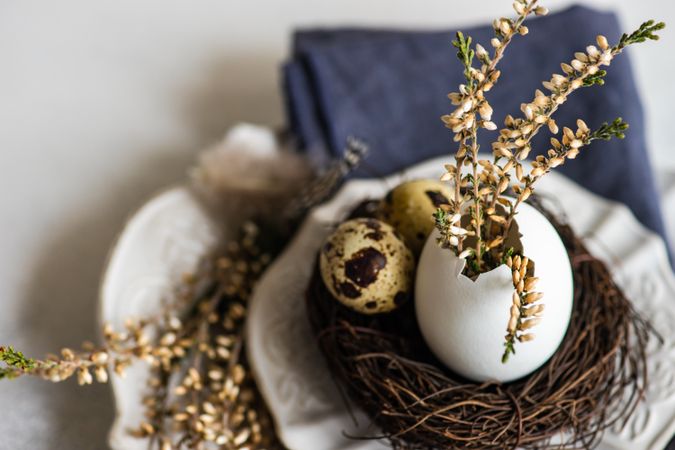 Easter table setting with decorative eggs, feather and heather on plates on grey counter with copy space