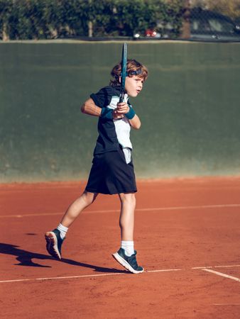 Sporty kid in activewear playing tennis with racket on court