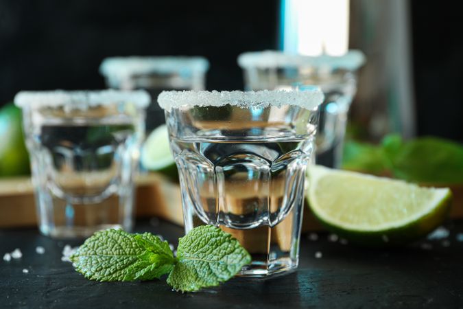 Tequila shots with salt, lime slices and mint on dark table