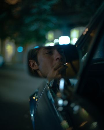 Young man's reflection on car rear mirror